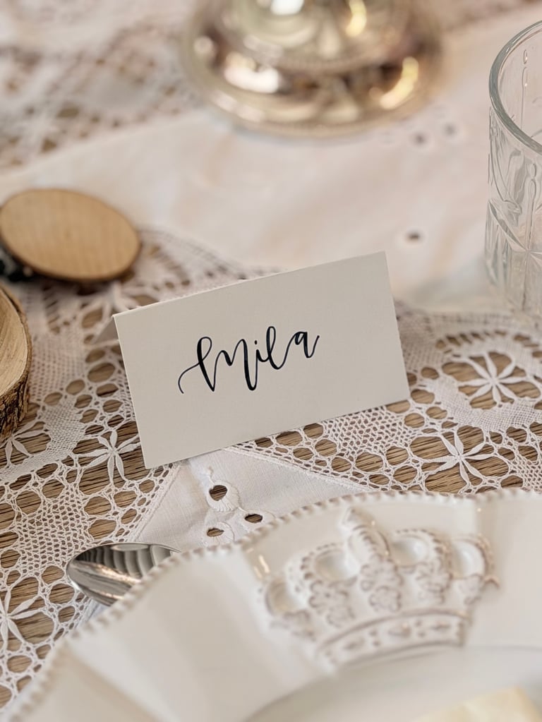 White place card with Ella written in calligraphy on an elegant table setting with lace tablecloth and white dinnerware