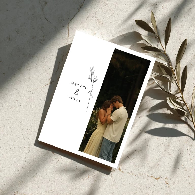 Wedding program or invitation with couple photo and dried olive branch on marble surface