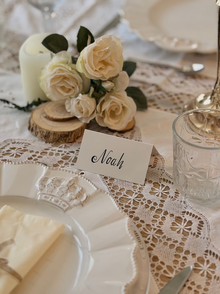 Elegant wedding place setting with peach roses, lace table runner, name card reading Noah, and white table décor