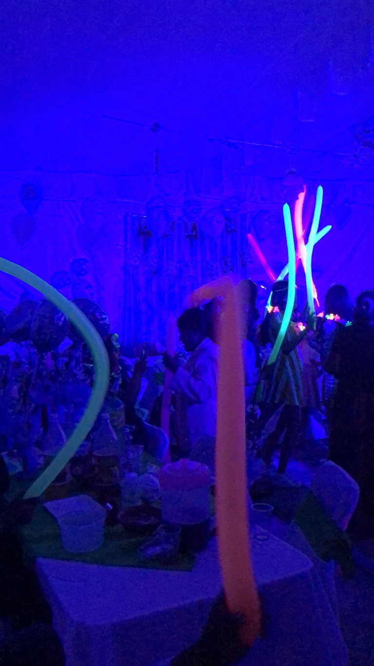 Neon glow-stick art installation at night event with crowd and purple-blue atmospheric lighting