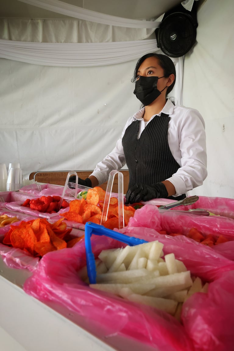 Person wearing black face mask and striped apron preparing fresh vegetables on pink table in commercial kitchen