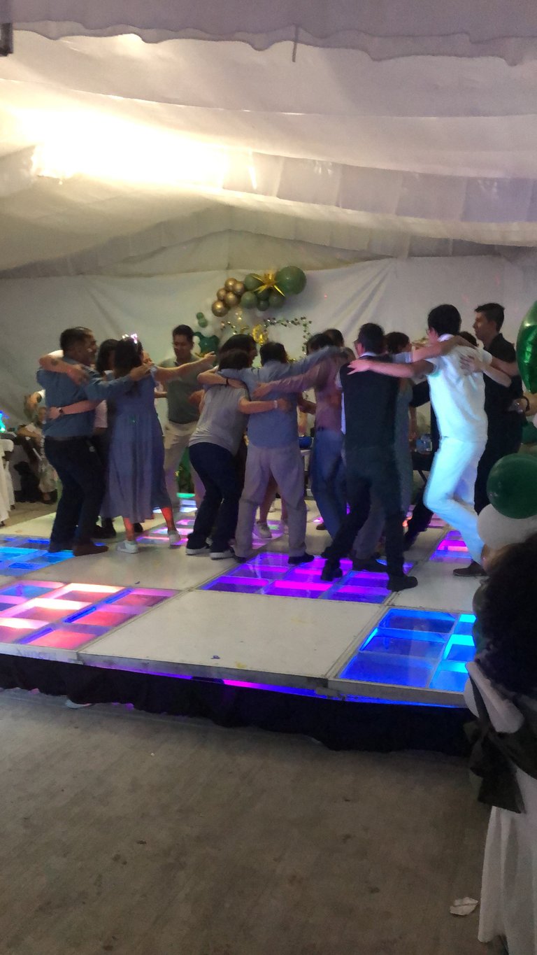 Group of people in formal attire dancing together on a neon-lit dance floor under a white tent at an event