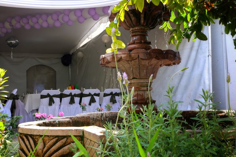 Decorative tiered stone fountain with hanging greenery in an event venue with purple balloons and decorated seating visible in background
