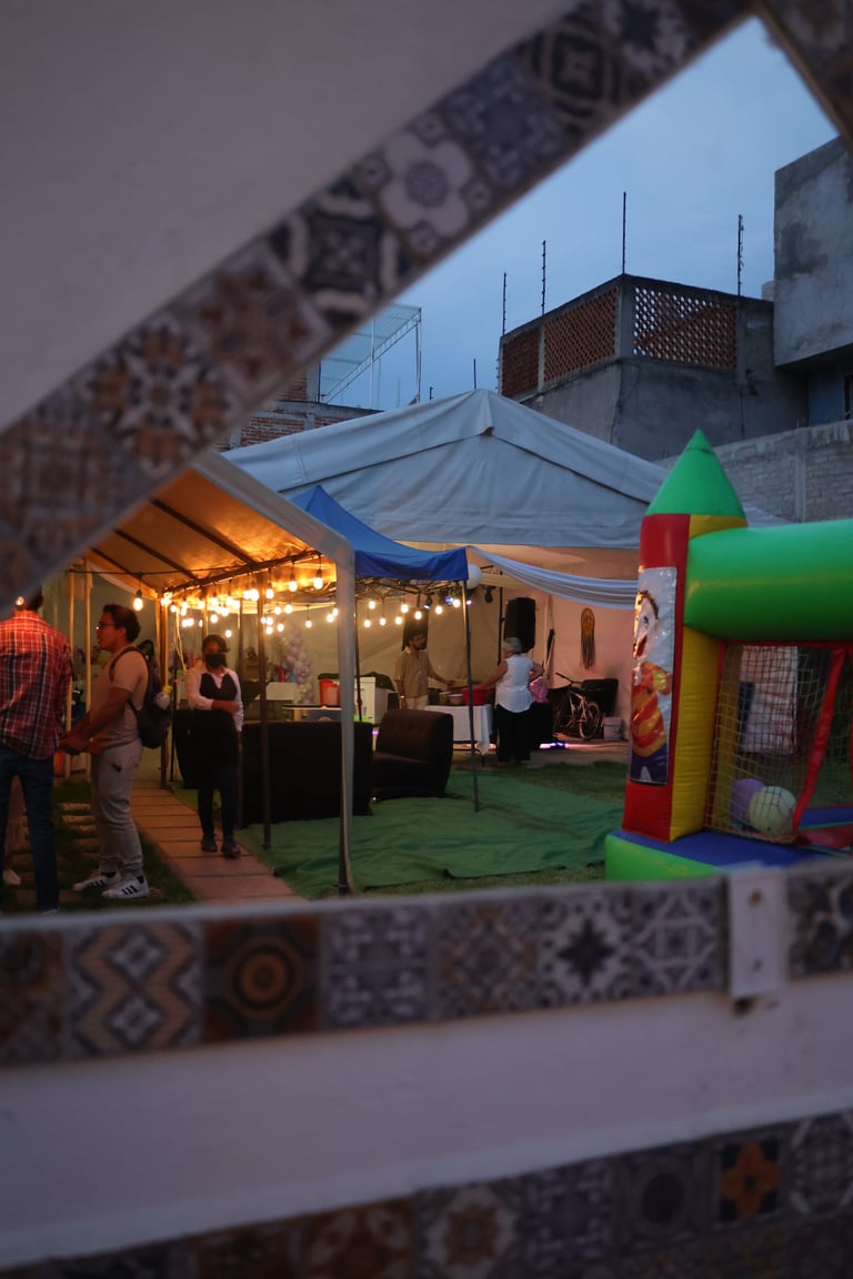 Evening rooftop event with illuminated tent, colorful bounce house, and people gathered under string lights on a decorated terrace