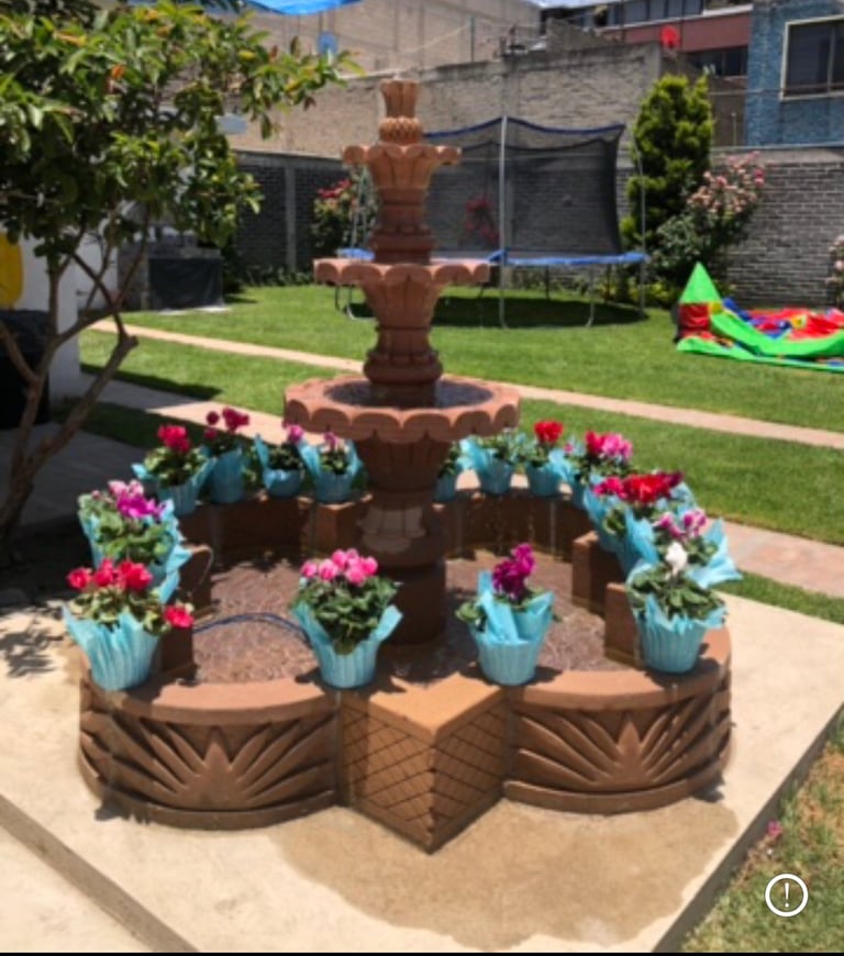 Decorative brown tiered fountain surrounded by turquoise pots of pink and red flowers in a backyard garden setting