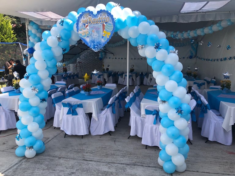 Blue and white balloon arch entrance with castle centerpiece at an indoor party venue decorated with tables and blue chair sashes