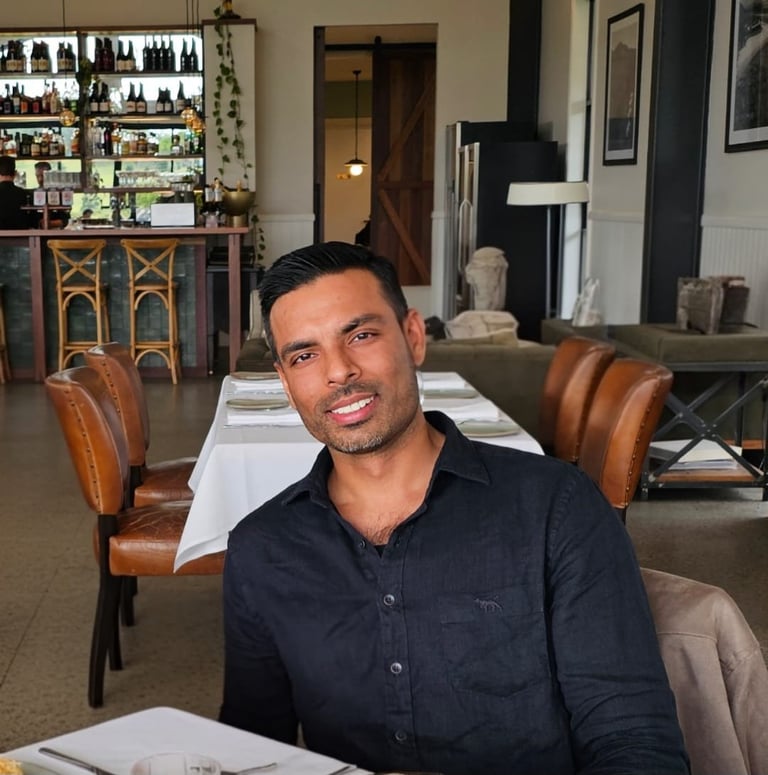Man in dark button-up shirt seated at dining table in upscale restaurant or lounge interior