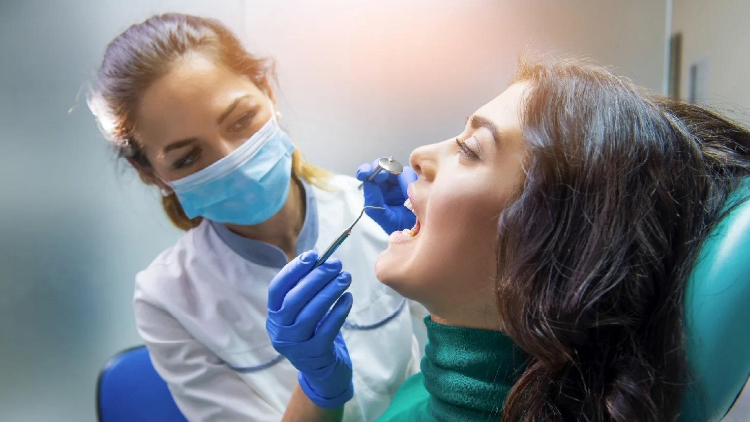 Dentist in mask and gloves performing oral examination on female patient in dental clinic