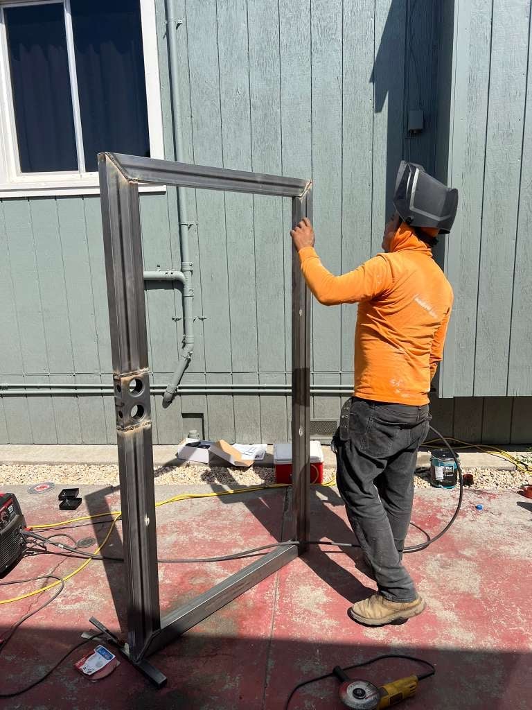 Worker in orange shirt welding a metal frame structure outdoors
