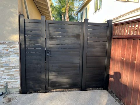 Black horizontal slat driveway gate with center door in residential setting