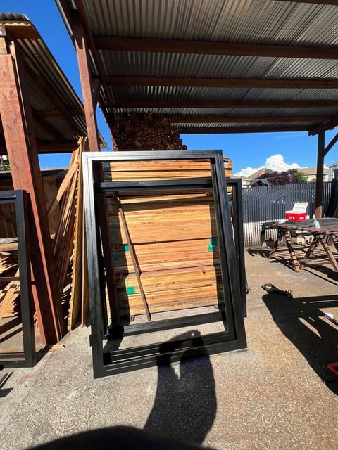 Wooden gate with black metal frame leaning against metal structures in an outdoor industrial yard under clear blue sky