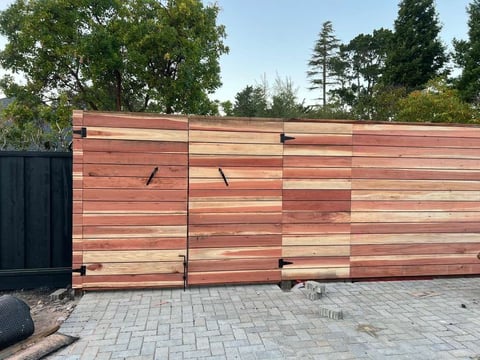 Modern wooden gate with horizontal red and natural wood panels, black metal frame