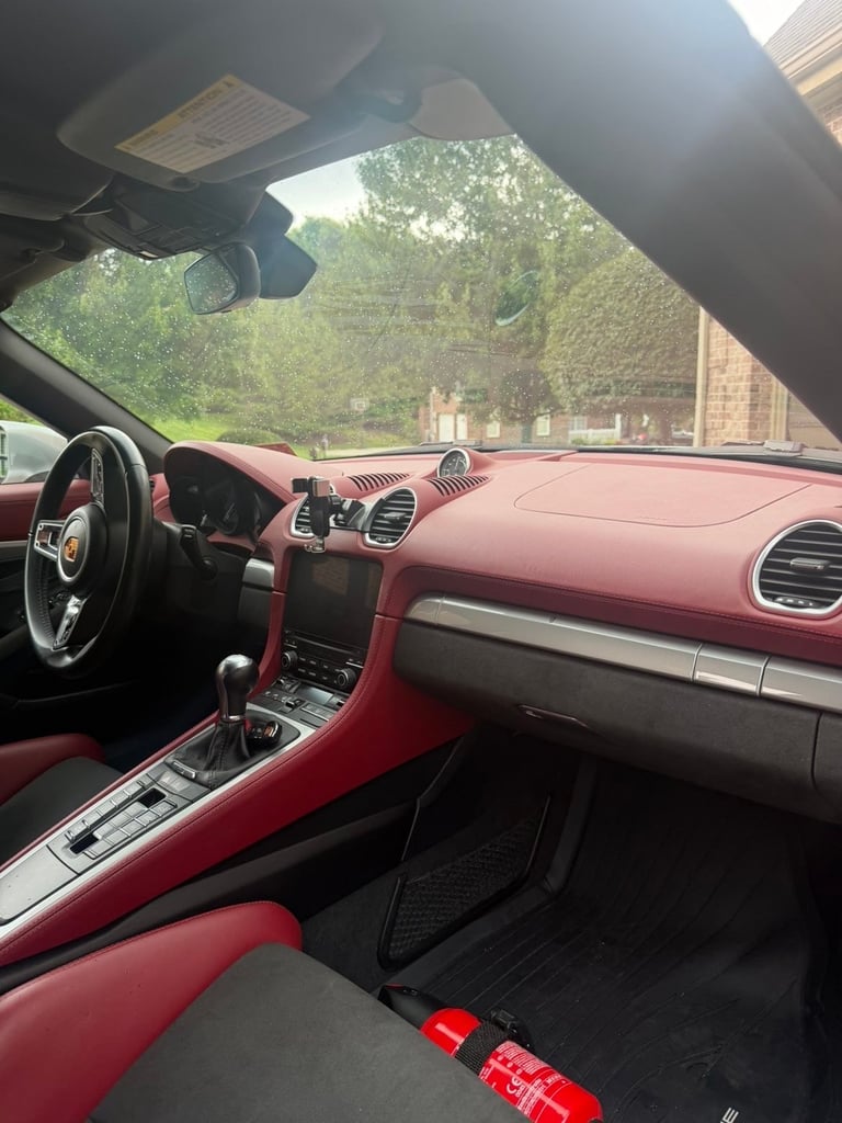 Interior view of a red sports car with dashboard, steering wheel, and convertible top down, trees visible through windshield