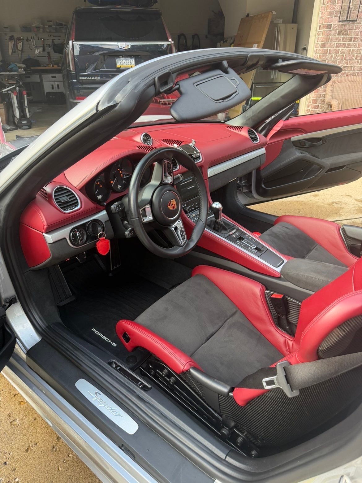 Red and black convertible sports car interior with open top, showing steering wheel, dashboard, and seats in a garage