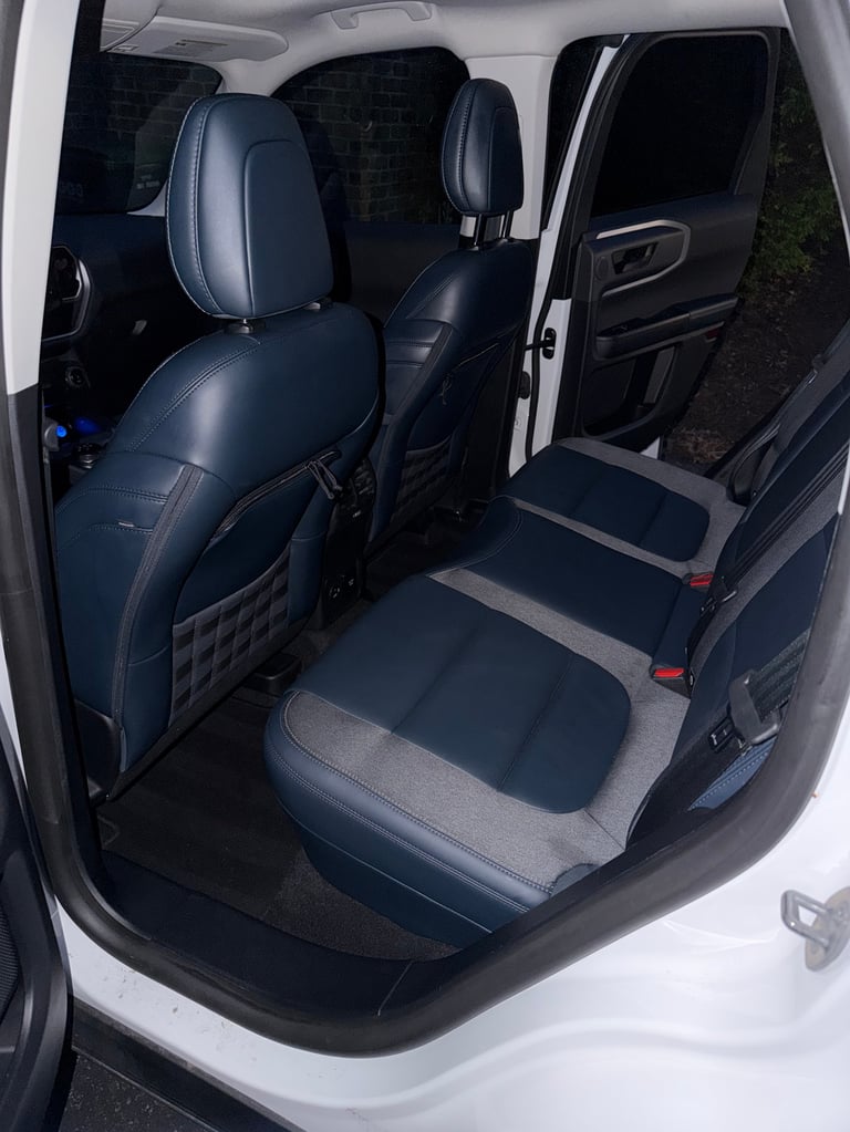 Interior view of a white vehicle with dark blue leather front seats and gray rear bench seat, door open showing seating arrangement