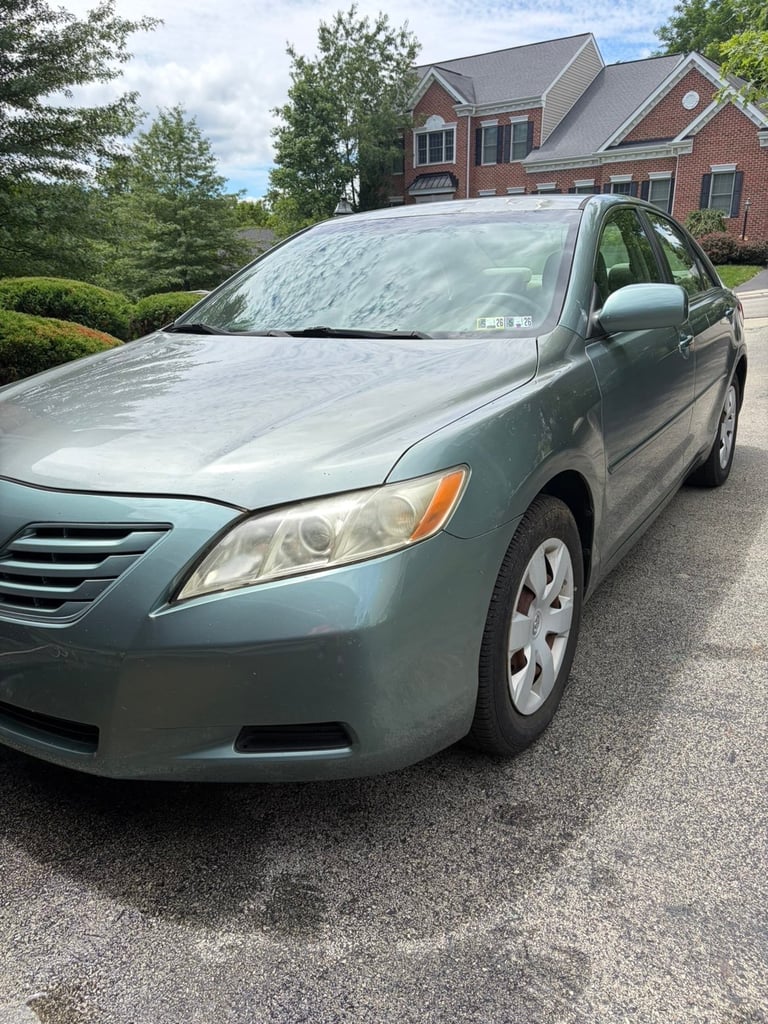 Silver Toyota Camry sedan parked in driveway in front of brick house with landscaping