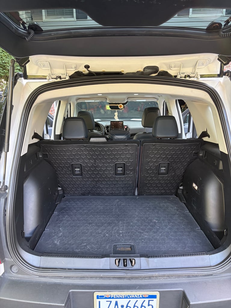 Open hatchback of a silver car showing empty cargo area with folded rear seats and black interior