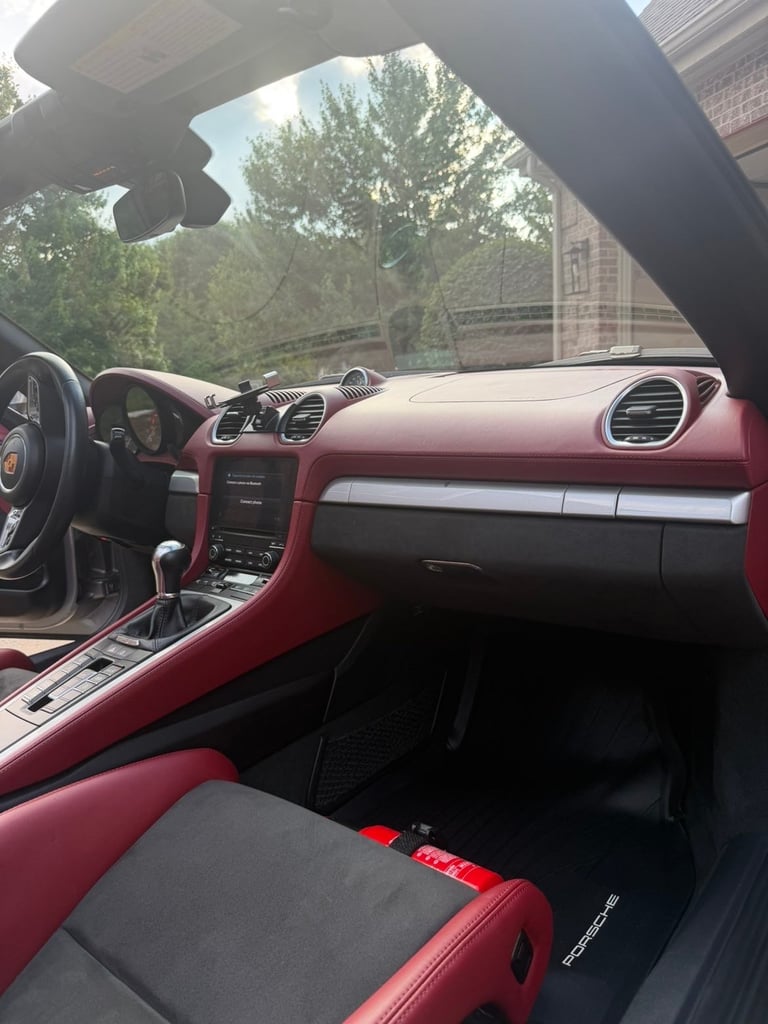 Interior of a red and black Porsche convertible with sunroof open, showing dashboard and steering wheel