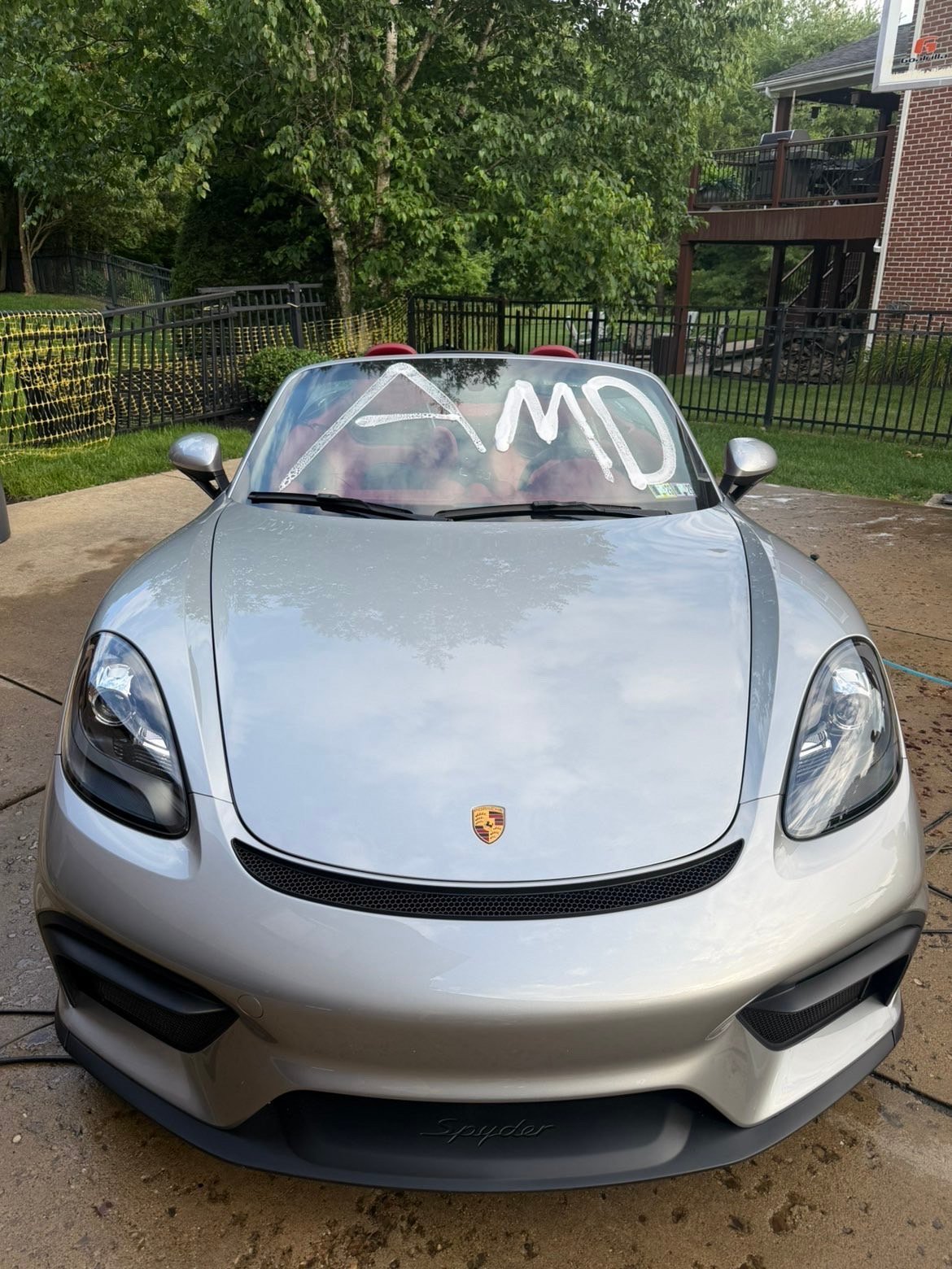 Silver Porsche sports car with white windshield banner parked in residential driveway