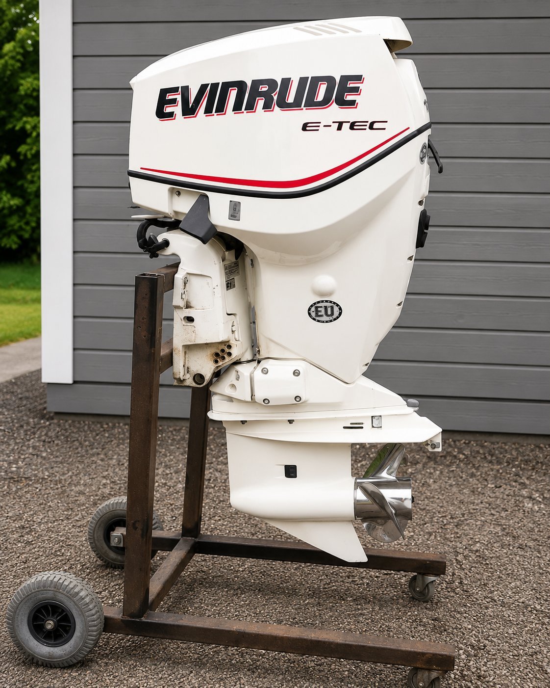 White Evinrude E-TEC outboard boat motor mounted on a wheeled stand against a gray shed.