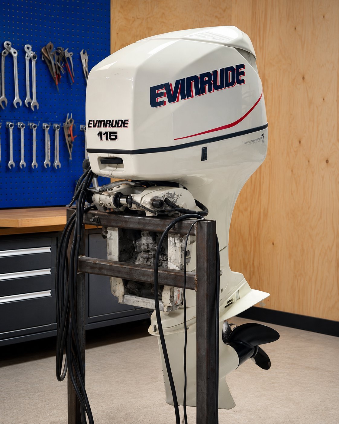Evinrude 115 horsepower outboard motor mounted on display stand in workshop with tools and storage visible in background.