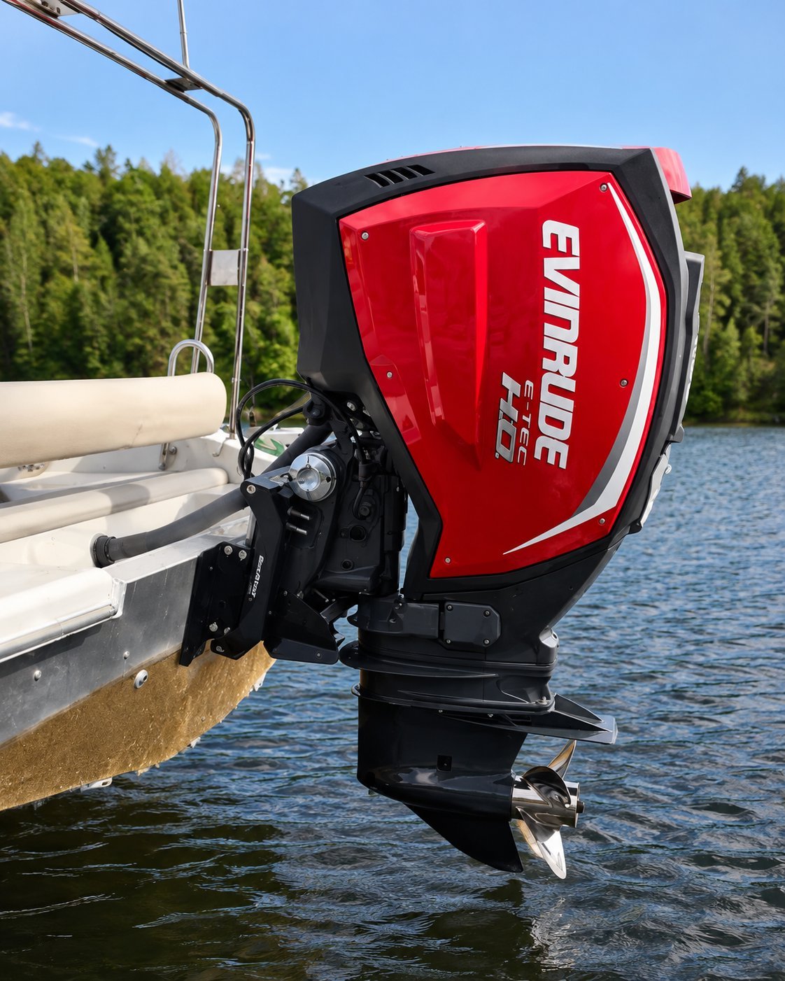 Red and black Evinrude outboard boat motor mounted on the back of a white and tan boat on a lake with forested shoreline in background.