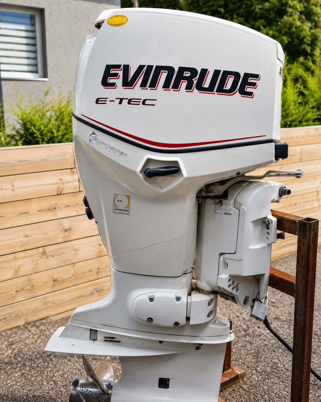 White Evinrude E-TEC outboard boat motor mounted on wooden dock with residential house in background.