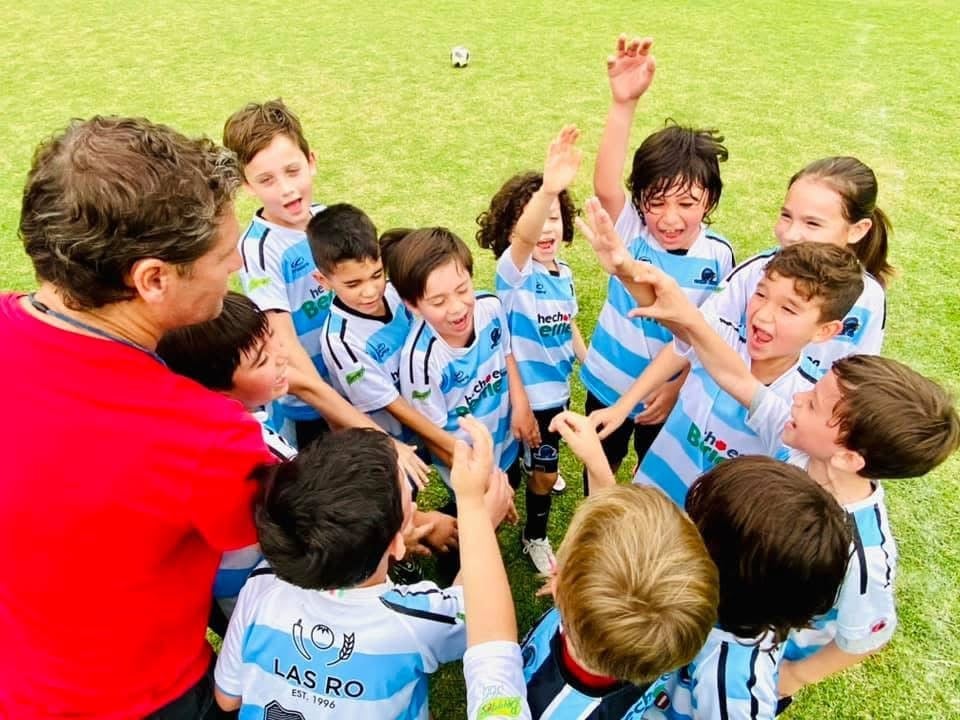 Youth soccer team in blue and white striped jerseys huddled with coach in red on grass field