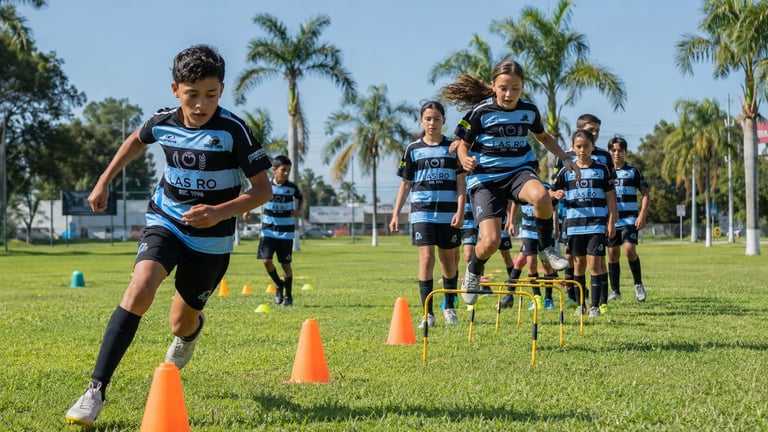 Young rugby players in blue and black striped jerseys running through training drills with cones on a grass field