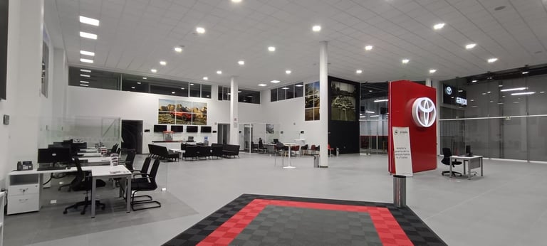 Modern Toyota dealership showroom with red and black entrance mat, bright ceiling lights, reception desk, and office spaces