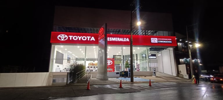 Night view of a Toyota dealership storefront with illuminated red signage and glass entrance doors.
