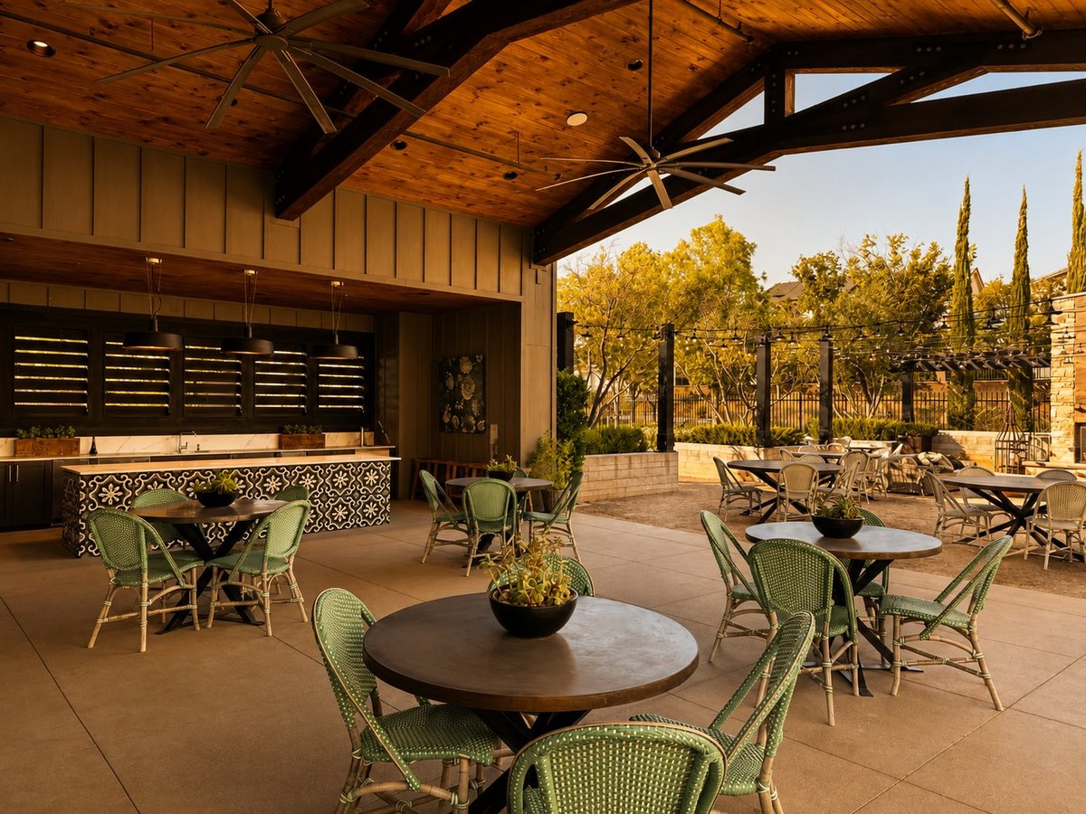 Elegant outdoor patio with covered pavilion, round tables, green chairs, bar area, and cypress trees at sunset