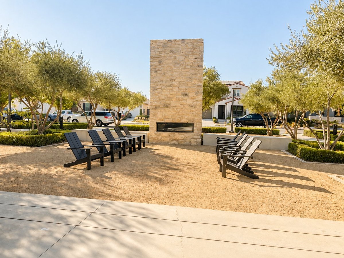 Public plaza with brick memorial monument, rows of metal chairs, olive trees, and park benches