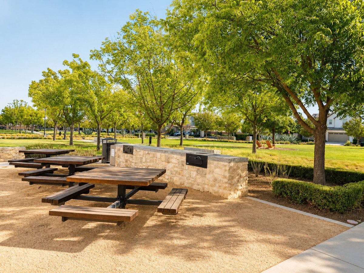 Outdoor picnic area with wooden tables and benches under large shade trees in a park setting