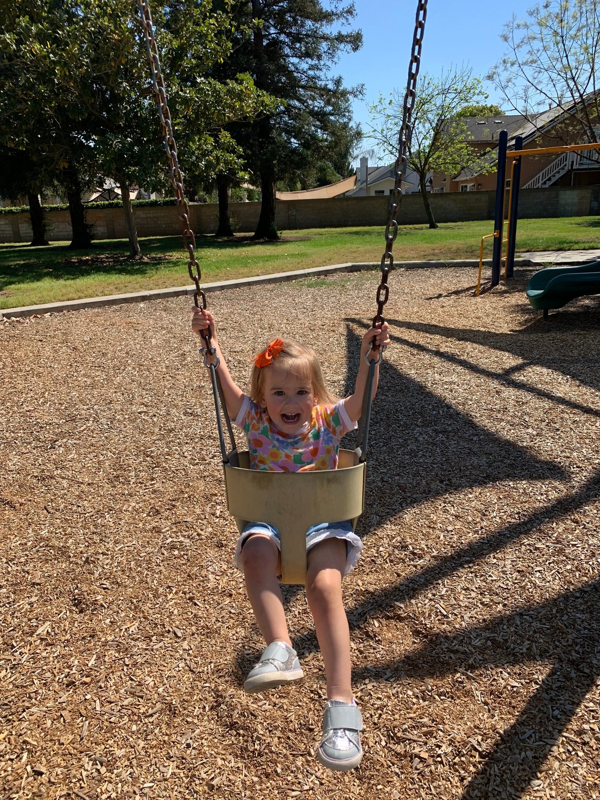 Young child with blonde hair swinging on a playground swing set at a park on a sunny day