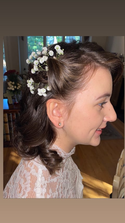 Profile view of a woman with dark hair styled in an updo adorned with white babys breath flowers and lace clothing