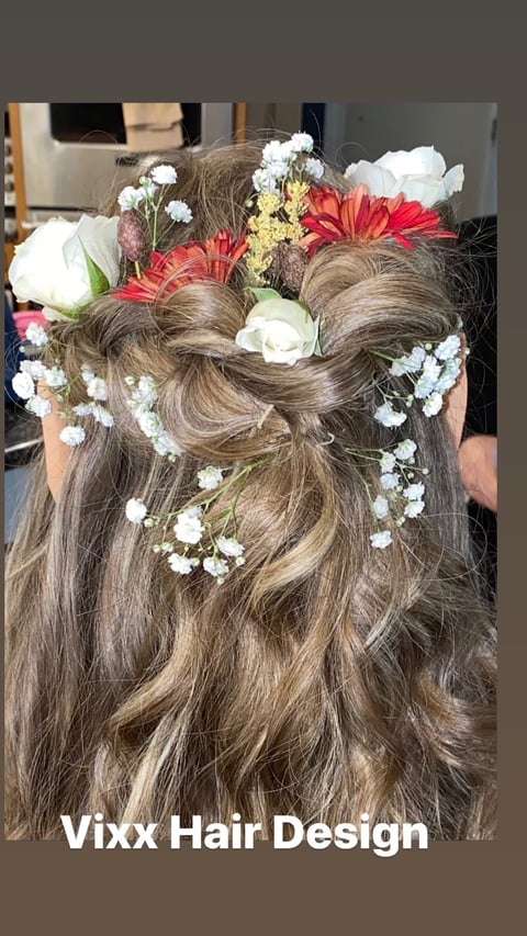 Long brown hair styled with half-up bow and decorated with white babys breath, red gerbera daisies, and white roses