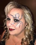 Woman with blonde wavy hair wearing artistic spider web face paint design on her cheek and forehead