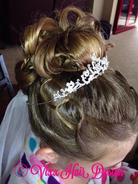 Childs updo hairstyle with blonde highlights, ornate crystal tiara, and tulle accessory, viewed from back