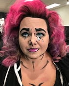 Person with bright pink curly hair and bold makeup wearing a black and white jacket