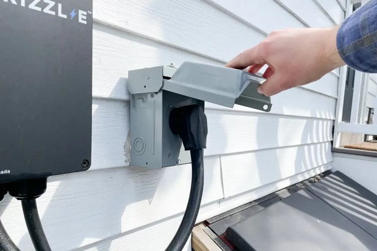 Person plugging in a power cord to an outdoor electrical outlet mounted on a white wall