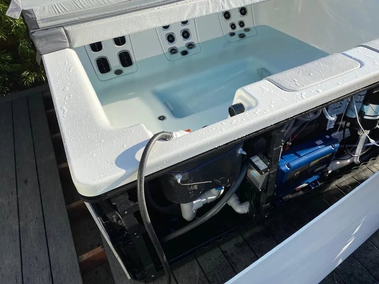 Overhead view of an open hot tub with jets, showing mechanical components and control systems underneath on a wooden deck