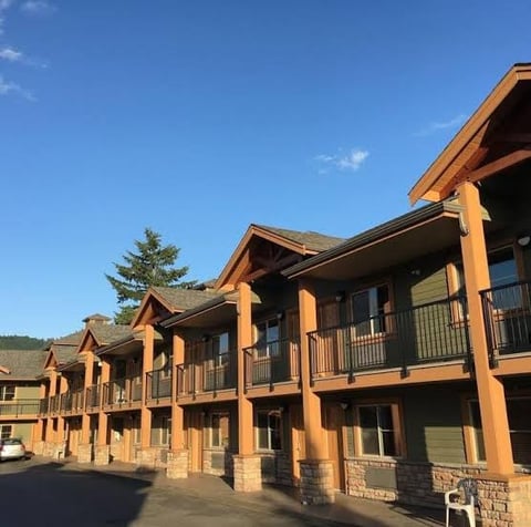 Row of rustic wooden lodge-style buildings with stone bases under clear blue sky and forested hillside backdrop — CN Electrical tourism & hospitality electrical services for lodges, hotels, motels, and restaurants in Chilliwack, BC