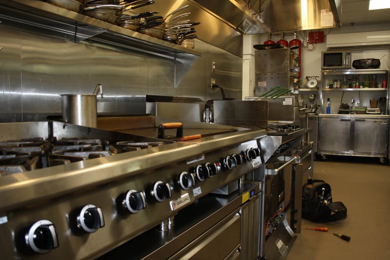 Professional kitchen with stainless steel range, hood, and cooking equipment in an institutional or commercial setting