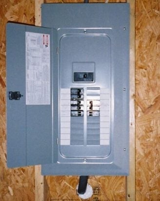 Open electrical panel mounted on wall showing circuit breakers and wiring