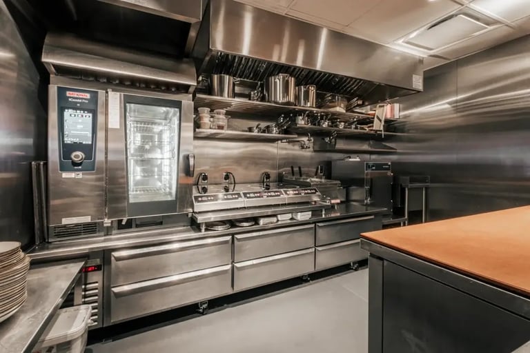 Professional stainless steel kitchen with cooking equipment, shelving, and wood-topped counter
