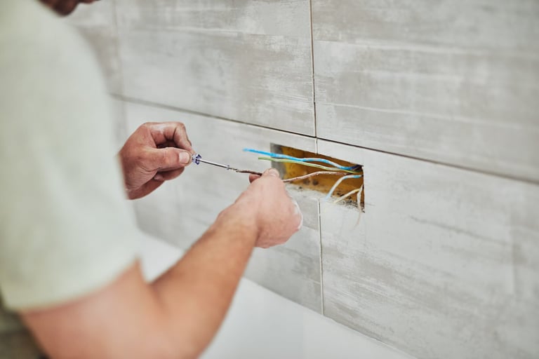 Person installing a gold-colored electrical outlet or switch into a white subway tile wall using a screwdriver