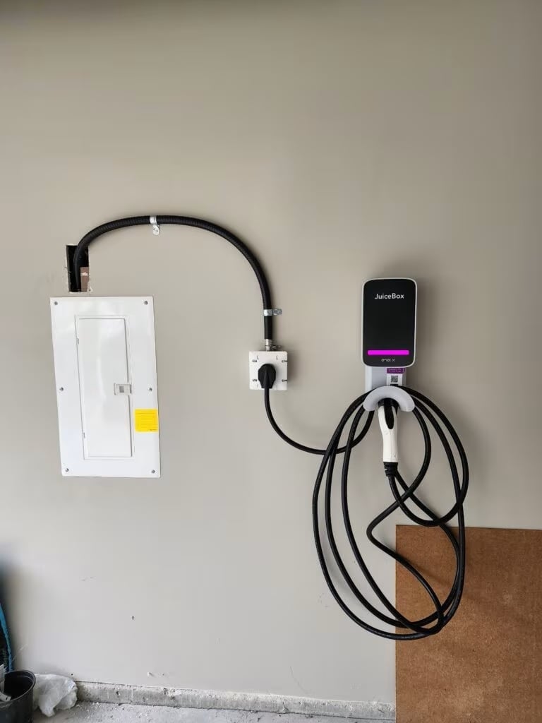 Wall-mounted electric vehicle charging station with display screen, connected to white outlet panel by black cable