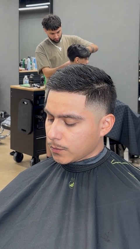 Barber styling a clients hair in a salon, focusing on the high fade and textured top haircut