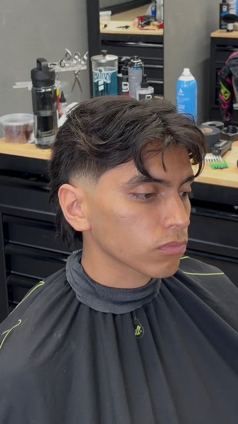 Man with dark textured hair and fresh fade haircut wearing black barber cape in salon setting